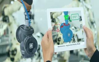 ine Person hält ein Tablet, das eine erweiterte Realität (Augmented Reality) Ansicht eines industriellen Bauteils zeigt, um Wartungsinformationen im Rahmen der industriellen Instandhaltung anzuzeigen