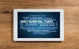 Ein Tablet liegt auf einem Holztisch und zeigt eine Wortwolke mit Begriffen rund um Instandhaltungsstrategien.
